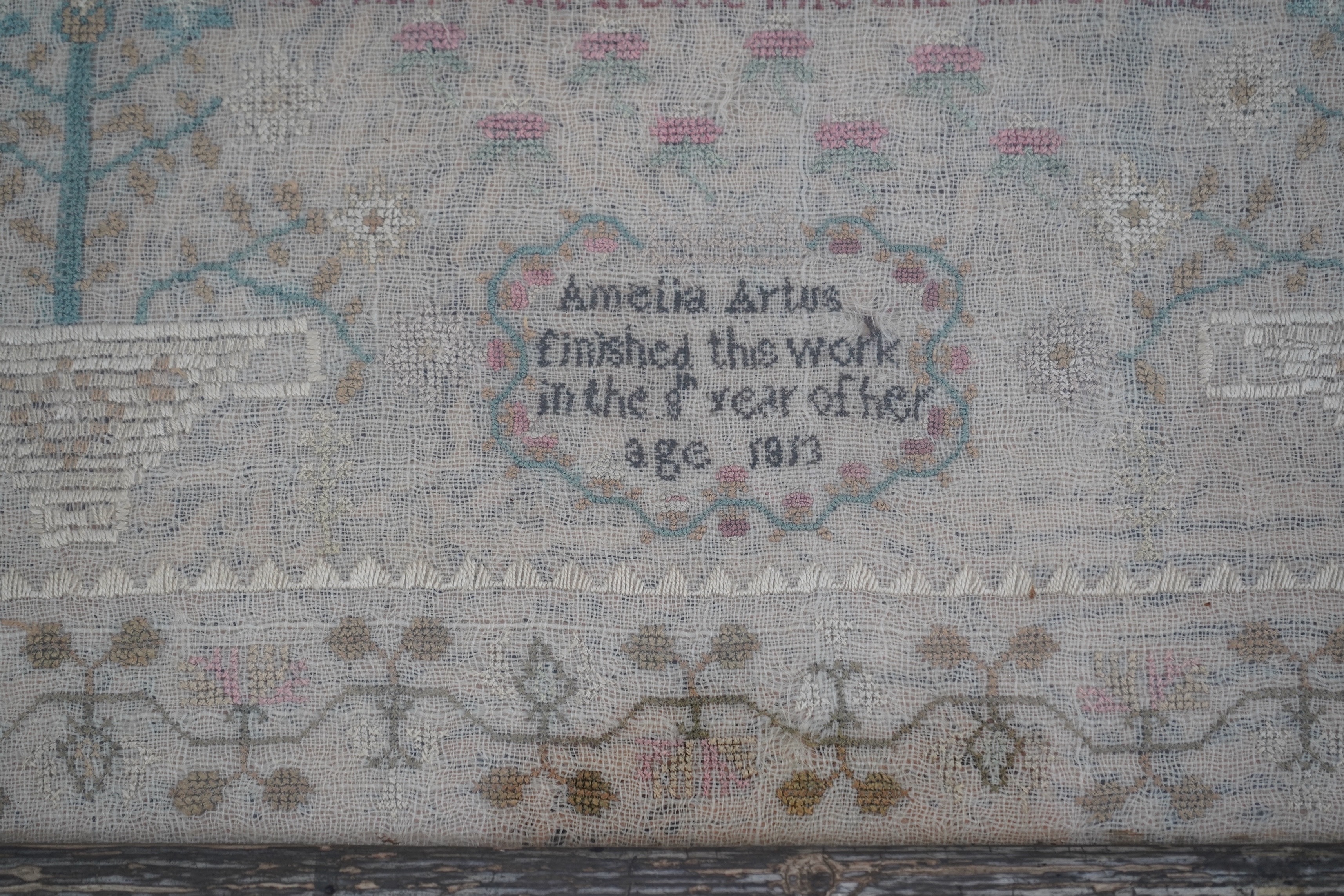 A gilt framed finely worked Regency gauze sampler, by Amelia Artus, aged 8 years, dated 1813, worked on fine gauze with coloured silk threads, with a large central panel having a long verse, two motifs of cornucopia, pot